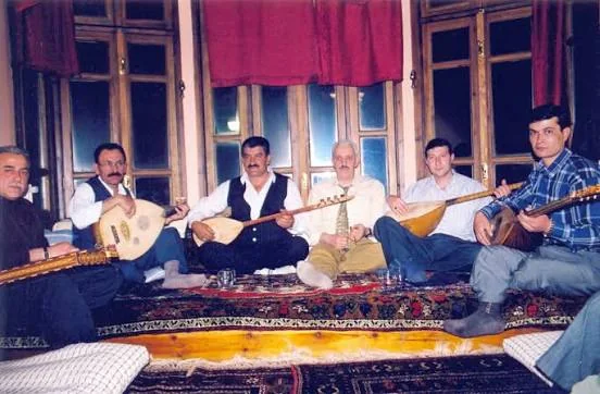 Kırmızı perdeli bir odada yer sofrasında sazlı sohbet