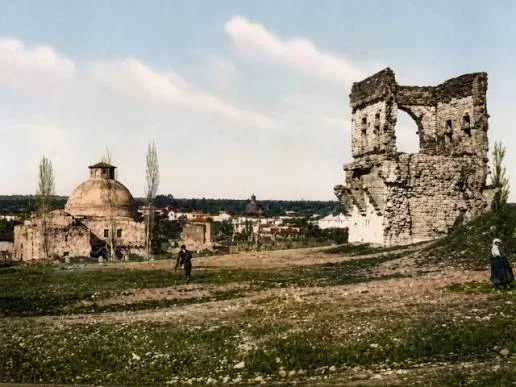 Tonlanmış eski bir fotoğrafta kubbeli bir yapı ve yıkık bir sur kulesi