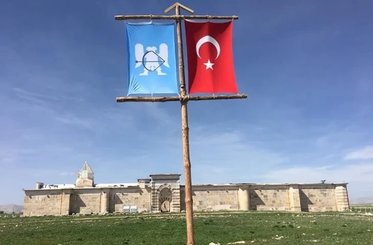 Zazadın Hanı önünde iki bayrak, arka planda taş bina