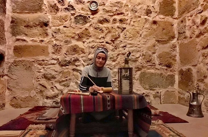 Dervişhane sahnesinde dönem kıyafetiyle yazı yazan kadın